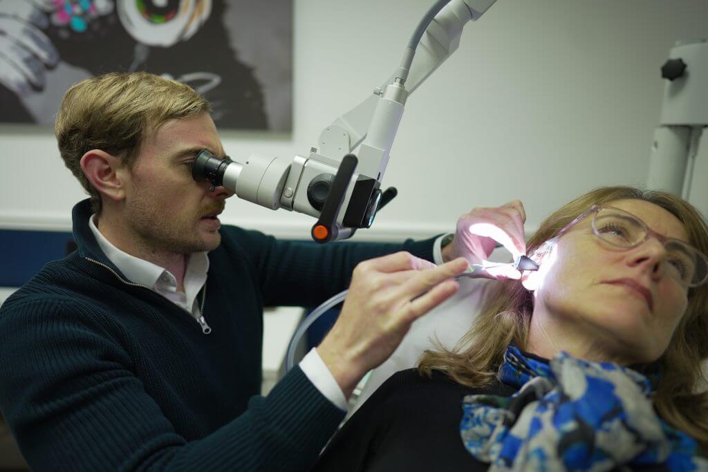 audiologist looking into someones ears in clinic room 3